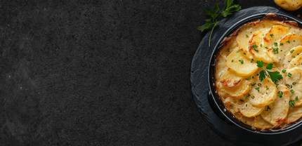 Fertiges Kartoffelgratin im Suppenteller auf Schieferhintergrund