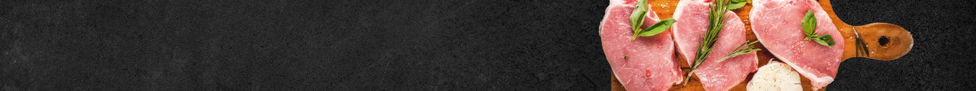 Schweine Steaks roh angerichtet auf Holzbrett und dekoriert mit Kräutern auf schwarzem Hintergrund