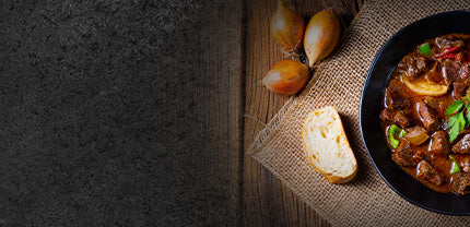 Fertiges Gulasch im Topf dekoriert mit einer Scheibe Baguette und gelben Zwiebeln schwarzer Hintergrund