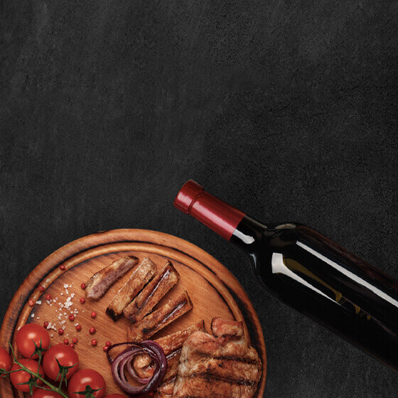 Für die perfekten Momente gebratenes Steak angerichtet auf Holzteller mit Zwiebeln und Tomatendeko und liegender Rotweinflasche