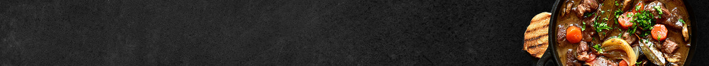 3 verschiedene Raclettepfannen gefüllt mit Tomaten Schinken Salami und Käse mit Meersalz und Pfeffer auf Schieferhintergrund