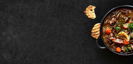 Gulasch in Sauce mit Möhren und Petersilie und Baguettescheiben auf Schieferhintergrund