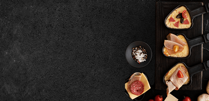 3 verschiedene Raclettepfannen gefüllt mit Tomaten Schinken Salami und Käse mit Meersalz und Pfeffer auf Schieferhintergrund