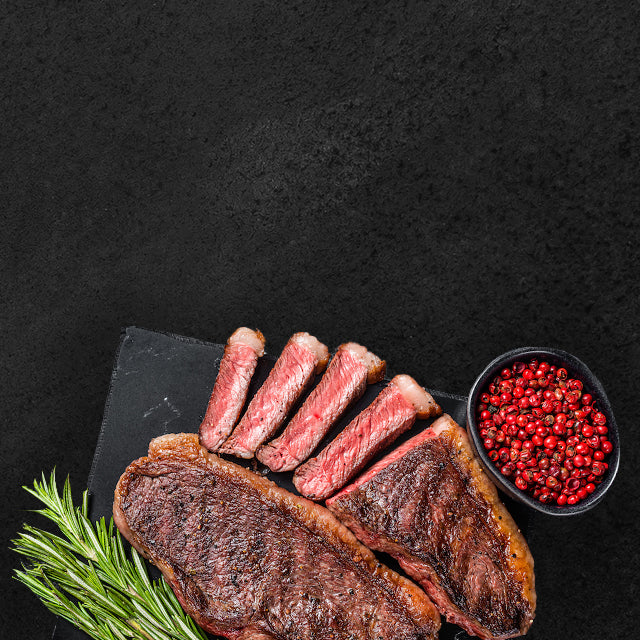 Gebratenes Rindersteak mit Anschnitt angerichtet auf Schieferplatte dekoriert mit rotem Pfeffer in einer Schale und Rosmarin