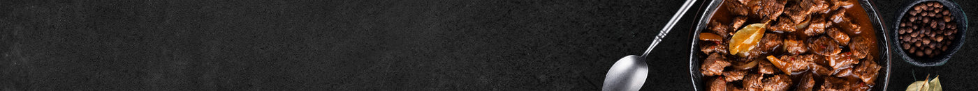 Rinder Gulasch in Gußpfanne gegart mit Löffel auf Schieferhintergrund