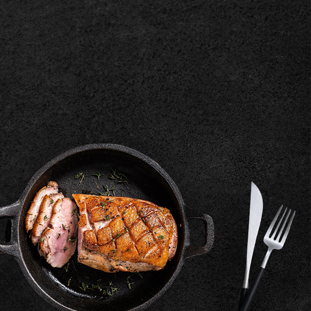 Krustenbraten im Topf und seitlich liegendem Besteck auf schwarzen Hintergrund