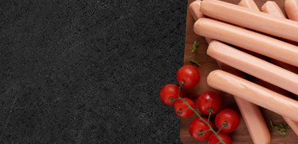 Siedewürstchen auf Holzbrett dekoriert mit Strauchtomaten auf schwarzem Hntergrund