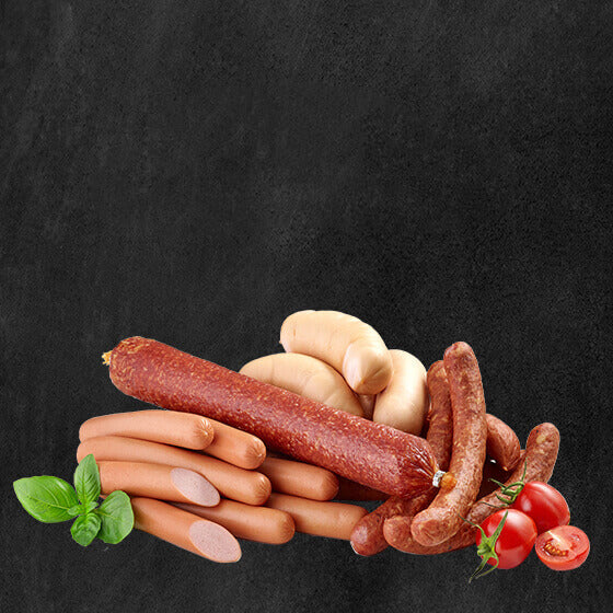 Verschiedene Würstchen und Salami angerichtet auf schwarzem Hintergrund dekoriert mit Tomaten und Basilikumblättern