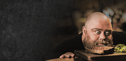 Mann mit Glatze der mit riesigen Augen auf ein Holzbrett guckt auf Schieferhintergrund