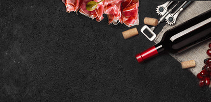 Roher Schinken mit Weinkorken einer Weinflasche und Flaschenöffner auf Schieferhintergrund