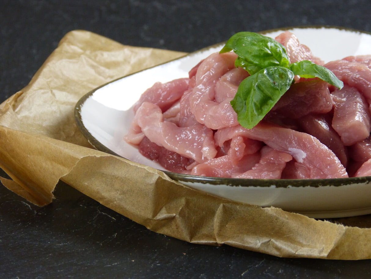 Schweinegeschnetzeltes natur mit Basilikumdeko auf Schieferhintergrund