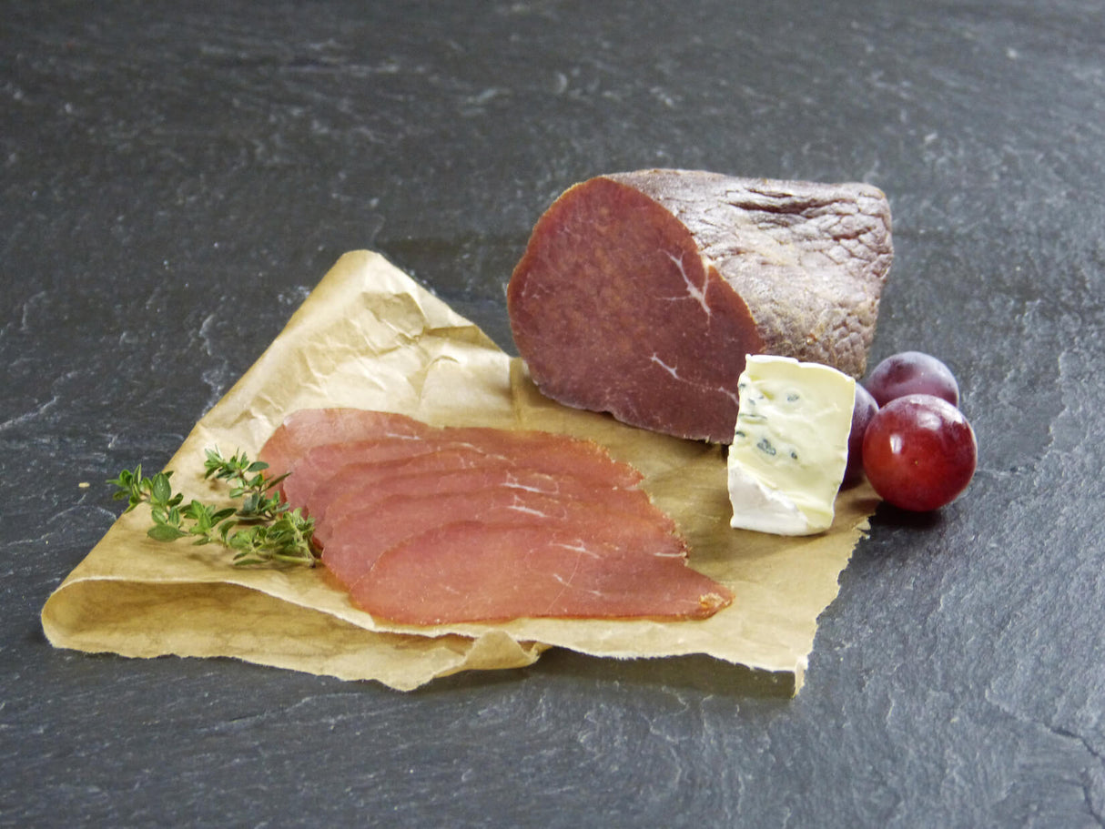 Rinder Rauchfleisch etwas in Scheiben aufgeschnitten mit Blauschimmelkäse und Trauben auf Schieferhintergrund