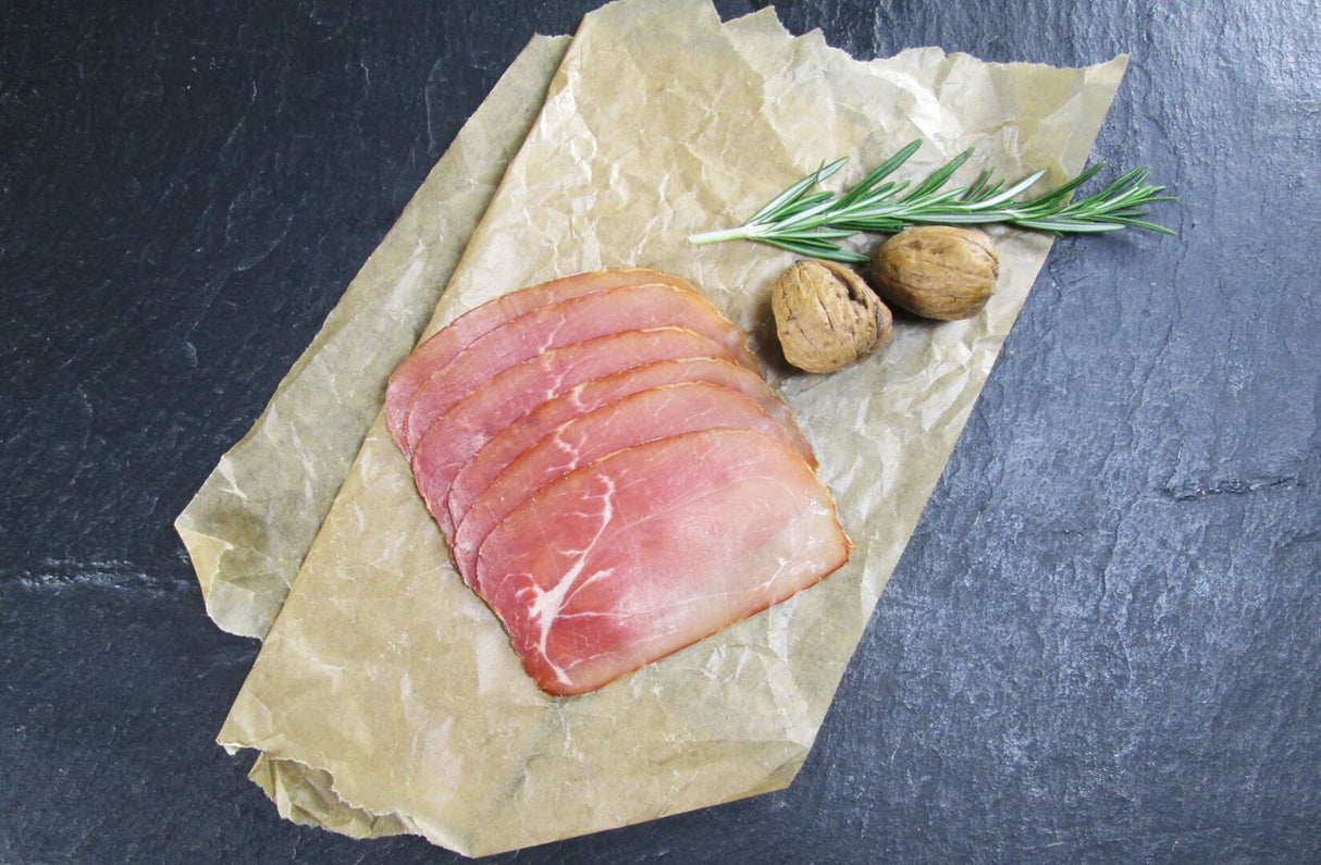 Nussschinken aufgeschnitten auf Backpapier angerichtet mit Kräutern auf Schieferhintergrund