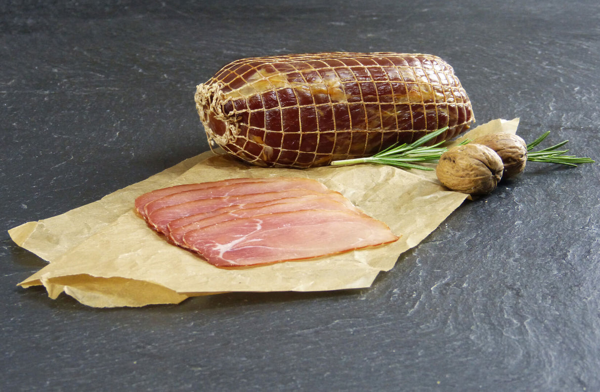 Nussschinken aufgeschnitten auf Backpapier angerichtet mit Kräutern auf Schieferhintergrund