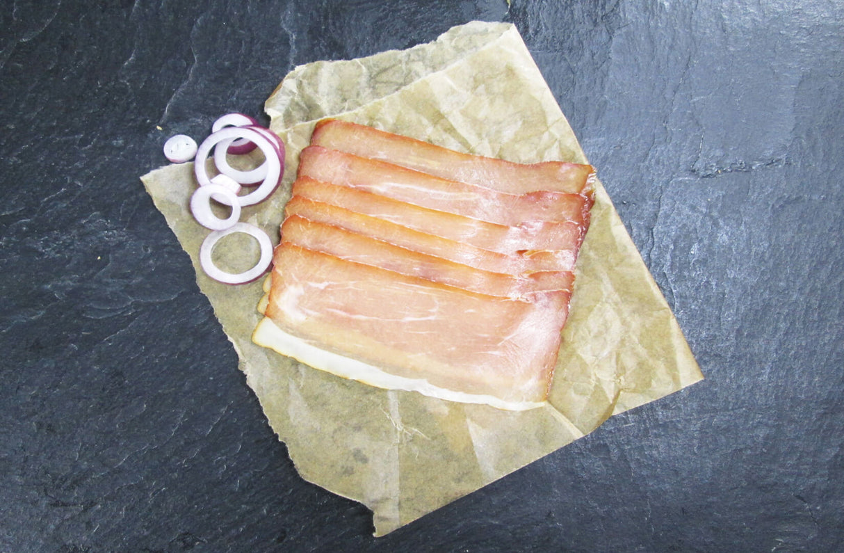 Schinkenspeckscheiben mit roten Zwiebeln auf Schieferhintergrund