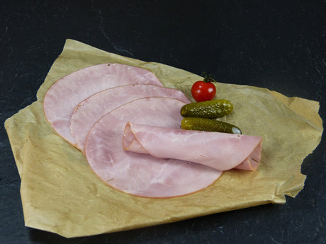 Gekochter Hinterschinken Kochschinken geschnitten mit Essiggurken und Tomaten auf Schieferhintergrund