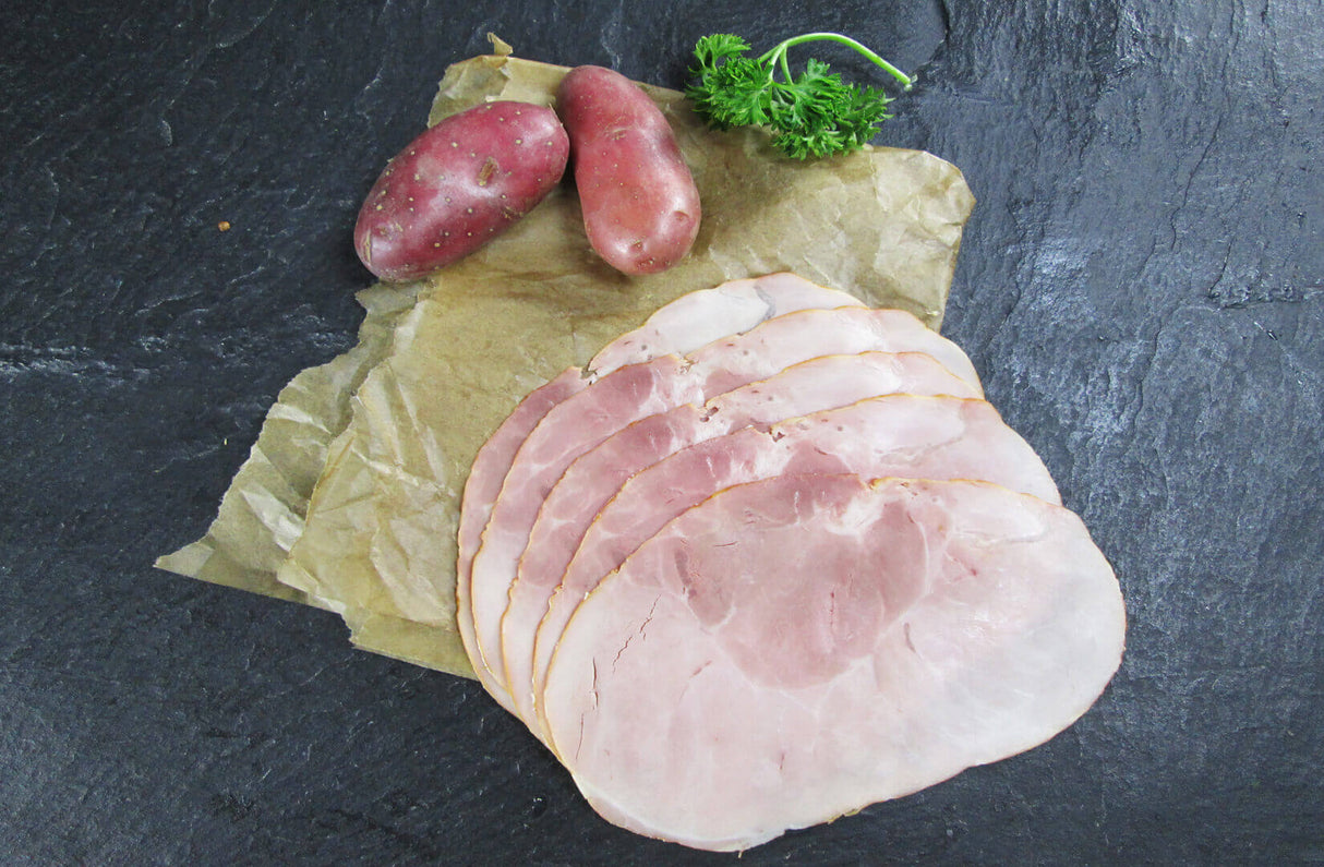 Gekochter Hüftschinken geschnitten und am Stück mit roten Kartoffeln und Petersilie auf Schieferhintergrund