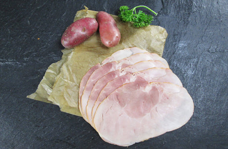 Gekochter Hüftschinken geschnitten und am Stück mit roten Kartoffeln und Petersilie auf Schieferhintergrund