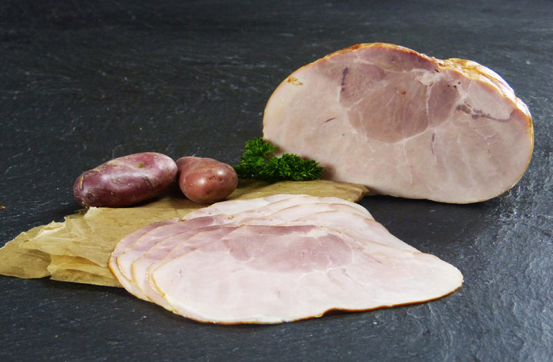 Gekochter Hüftschinken geschnitten und am Stück mit roten Kartoffeln und Petersilie auf Schieferhintergrund