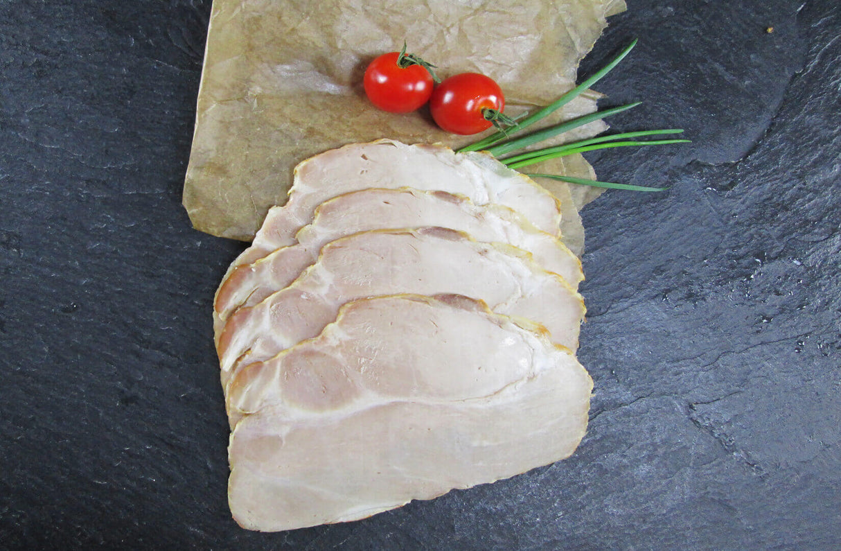 Schweinegrillbraten Aufschnitt angerichtet auf Backpapier mit Tomaten und Schnittlauch auf Schieferhintergrund