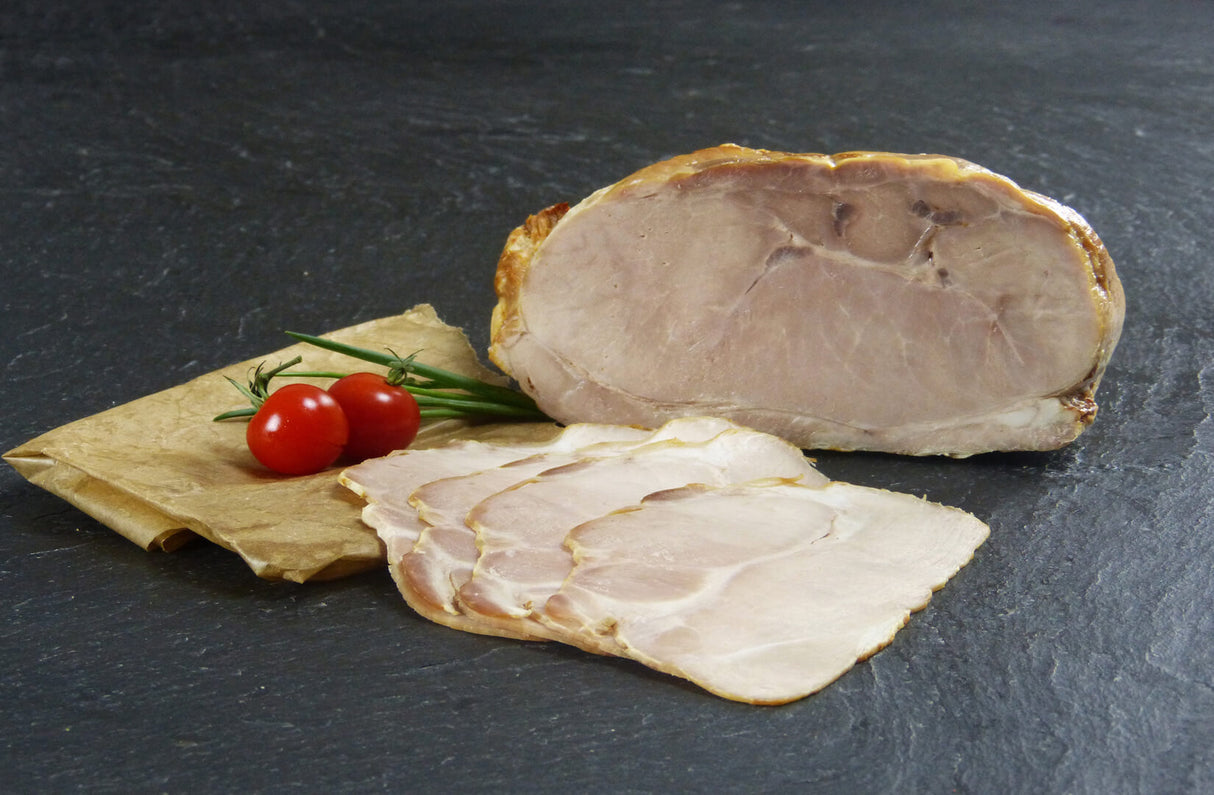 Schweinegrillbraten Aufschnitt angerichtet auf Backpapier mit Tomaten und Schnittlauch auf Schieferhintergrund