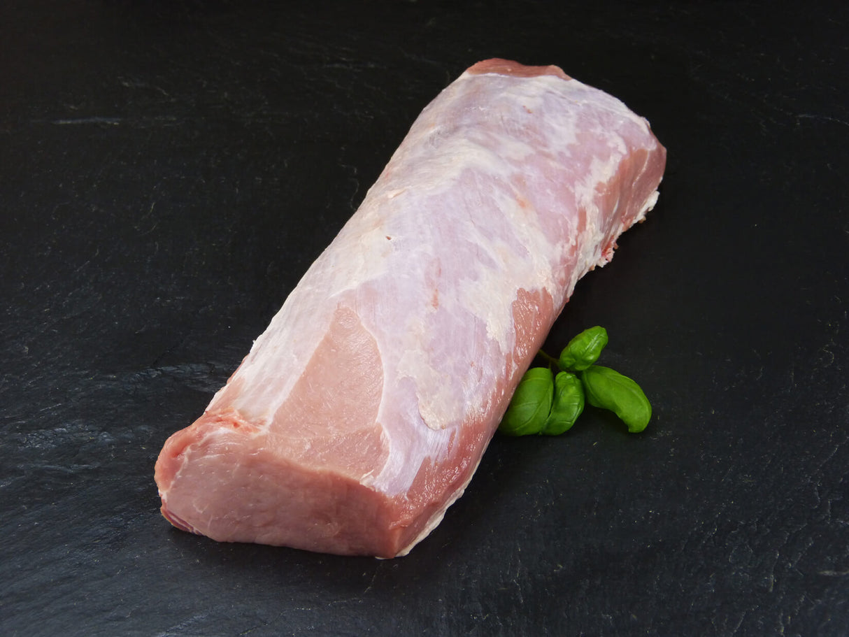 Schweinelachs am Stück mit Basilikum auf Schieferhintergrund schäg auf Schieferhintergrund