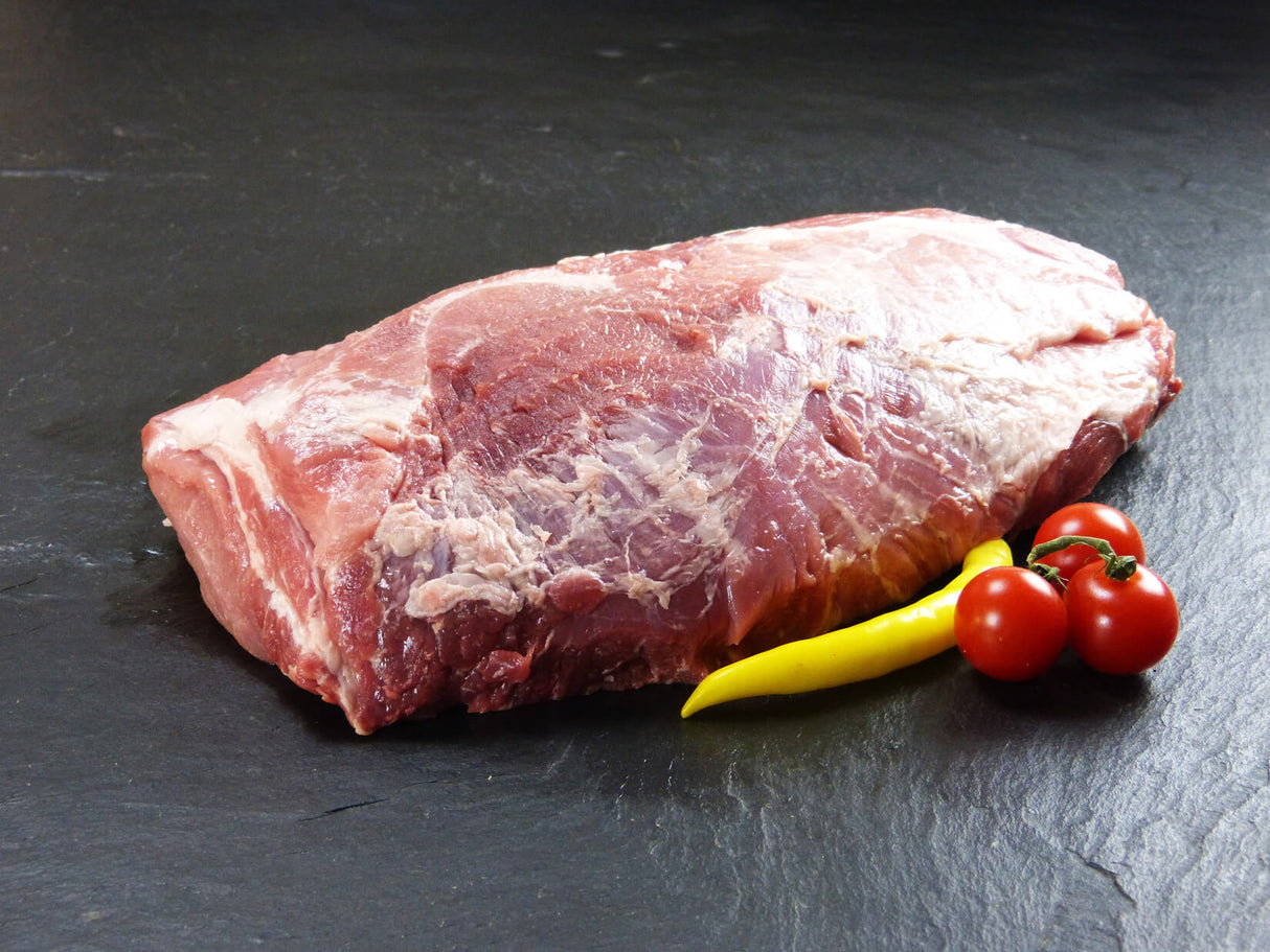 Schweinekamm ohne Knochen am Stück mit gelber Peperonie und Tomaten auf Schieferhintergrund