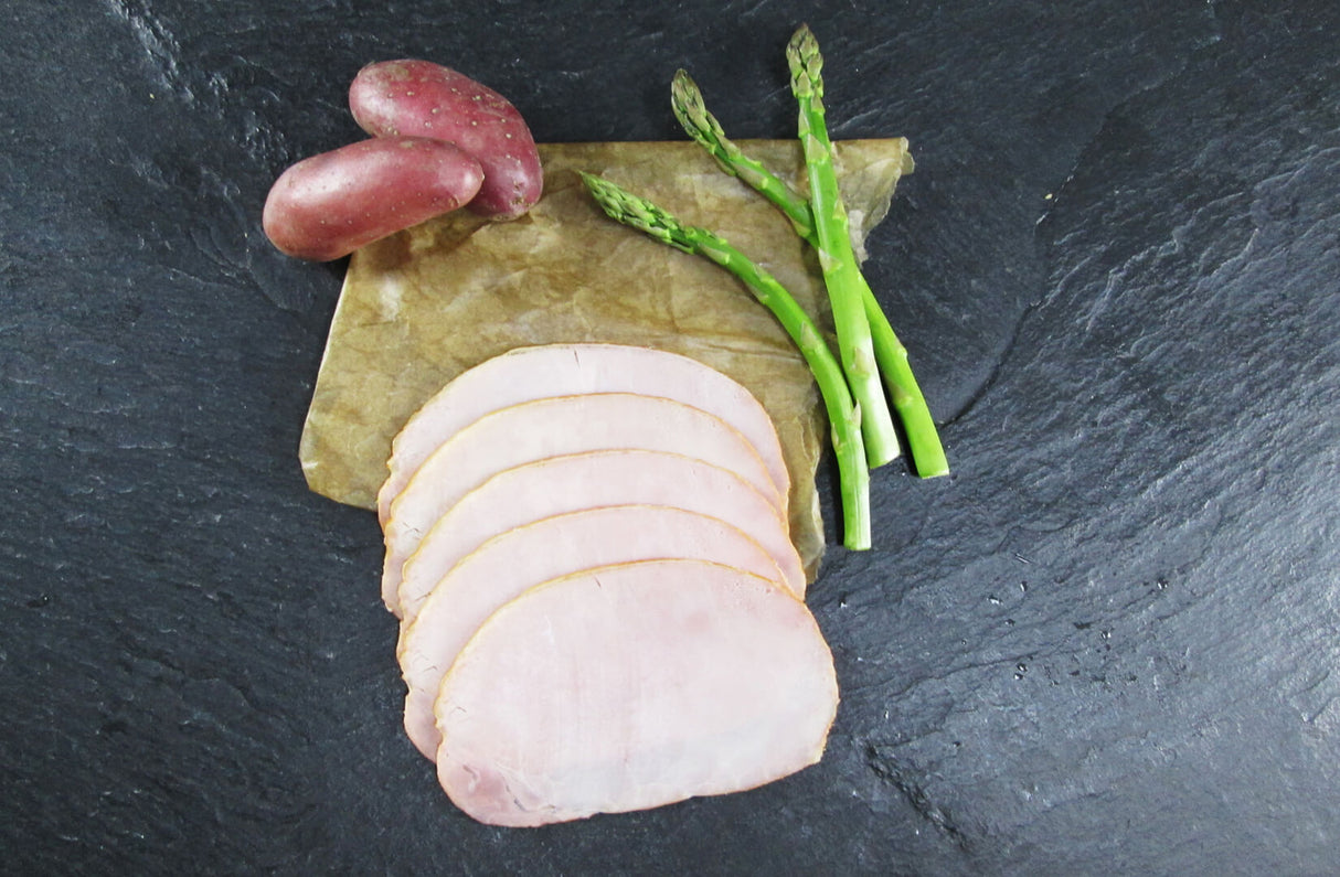 Kasseler ohne Knochen gekocht geschnitten mit roter Kartoffel und grünem Spargel auf Schieferhintergrund von oben fotografiert