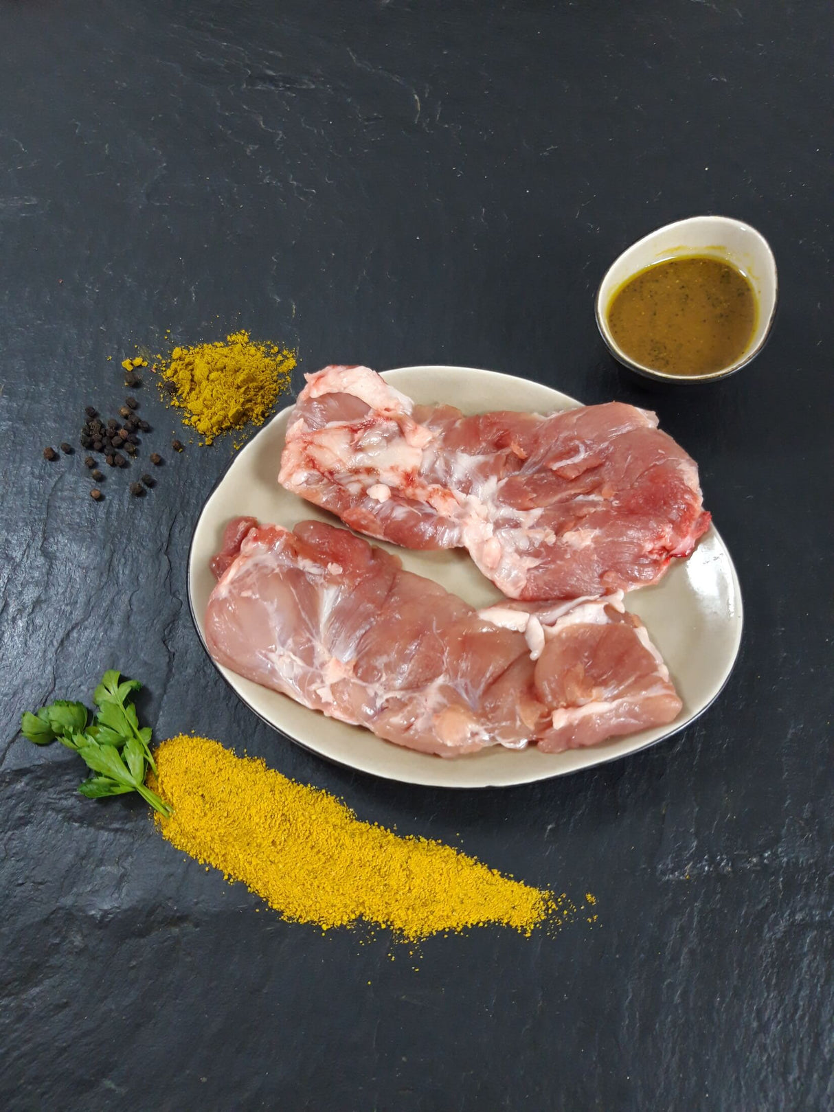 Spider Steak Kachelfleisch Bombay auf Teller angerichtet mit einer Schale Marinade Kräutern und Gewürzen auf Schieferhintergrund