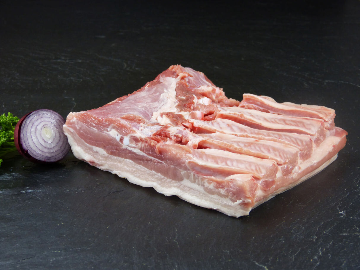 Schweinebauch ohne Rippe mit roter Zwiebel und Petersilie auf Schieferhintergrund