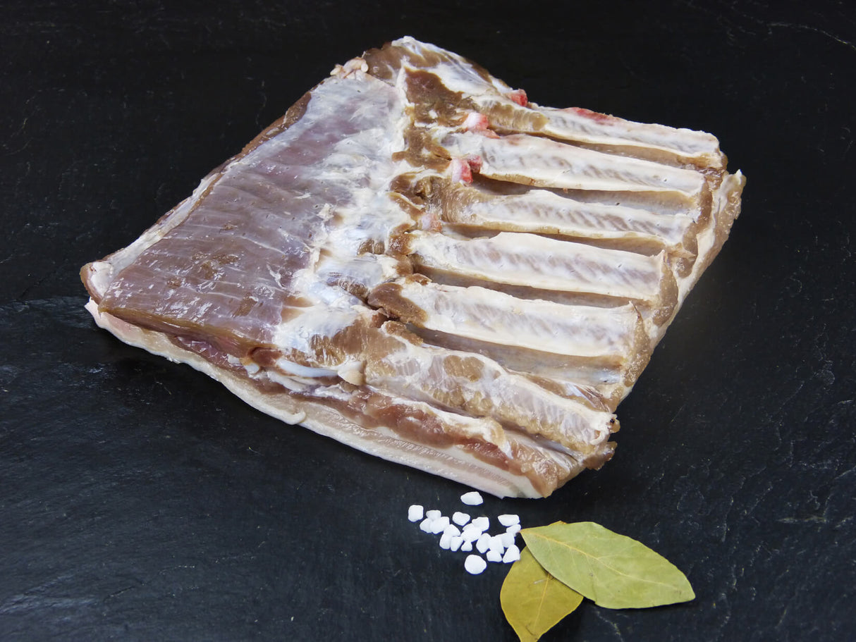 Schweinebauch ohne Rippe gepökelt mit grobem Salz und Lorbeeblättern auf Schieferhintergrund