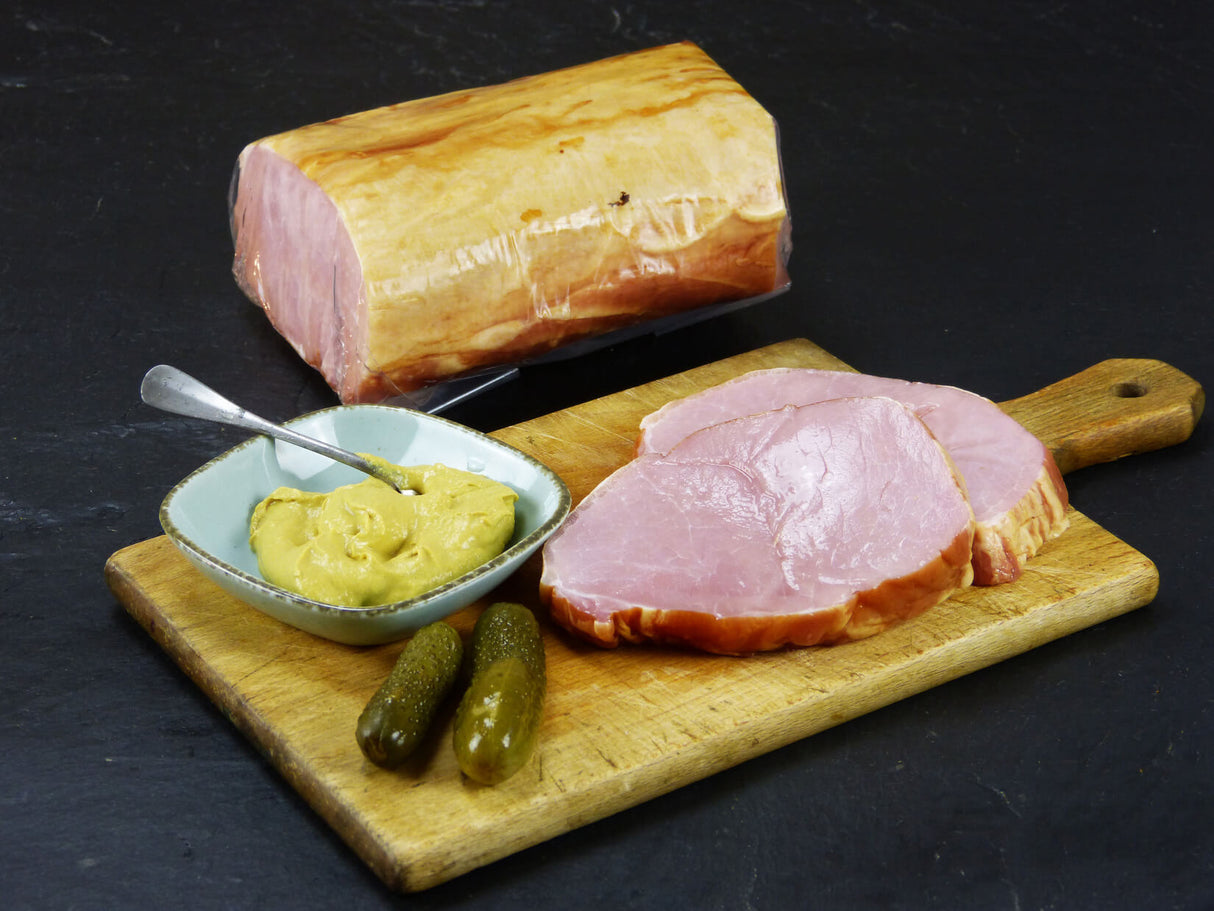 Kasseler Lachsbraten auf Holzbrett angerichtet mit Senf und Essiggurken auf Schieferhintergrund