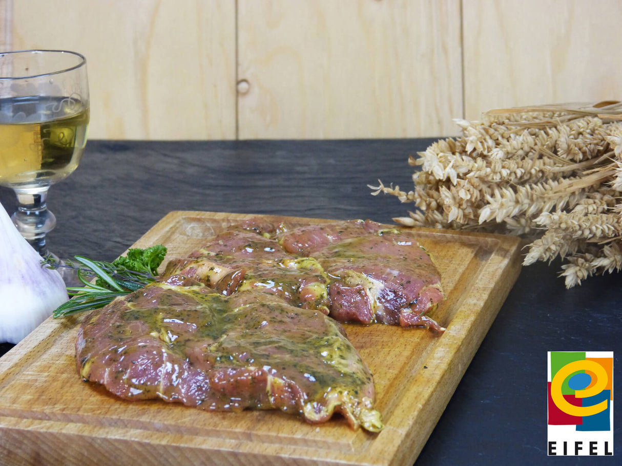 Kammsteak Kräuter Knoblauch vom EIFEL Schwein auf Holzbrett mit Ähren und Weinglas vor Holzwand