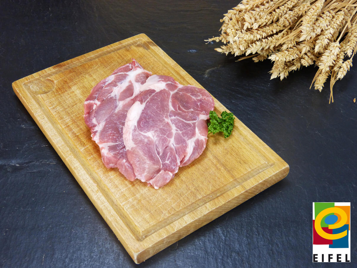 Kammsteak vom EIFEL Schwein auf Holzbrett mit Ähren auf Schieferhintergrund
