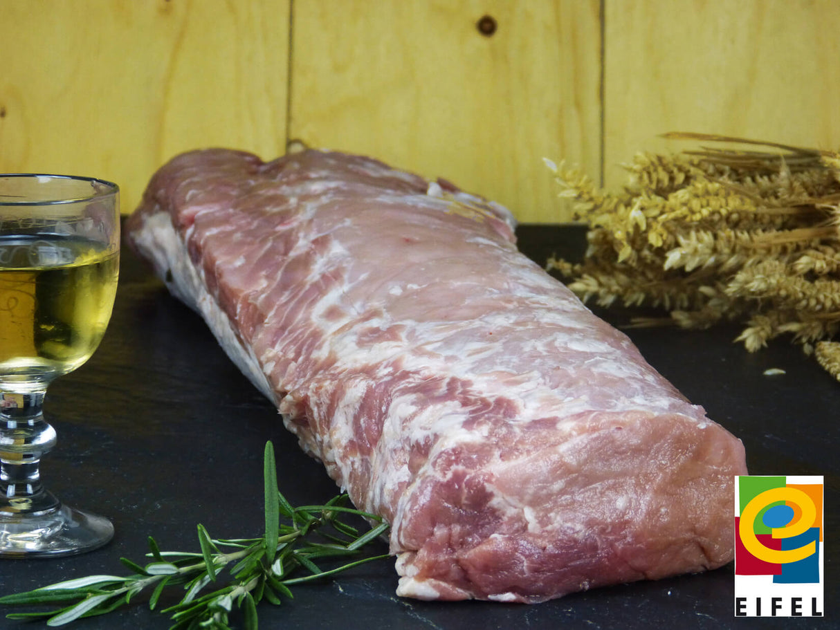 Schweinelachs vom EIFEL Schwein auf Holzbrett mit Ähren und Weinglas vor Holzwand