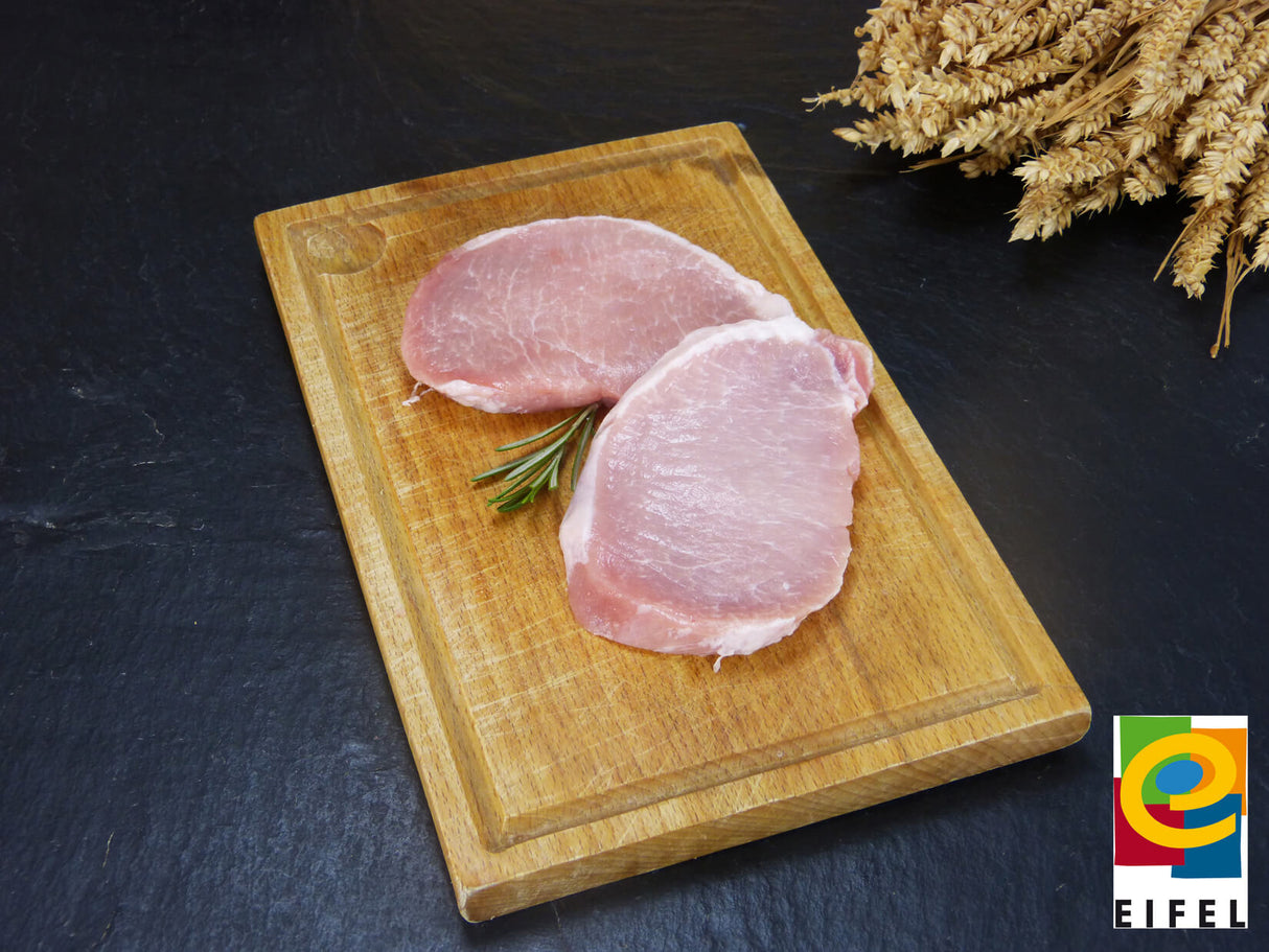 Rückensteak vom EIFEL Schwein auf Holzbrett mit Rosmarin und Ähren auf Schieferhintergrund