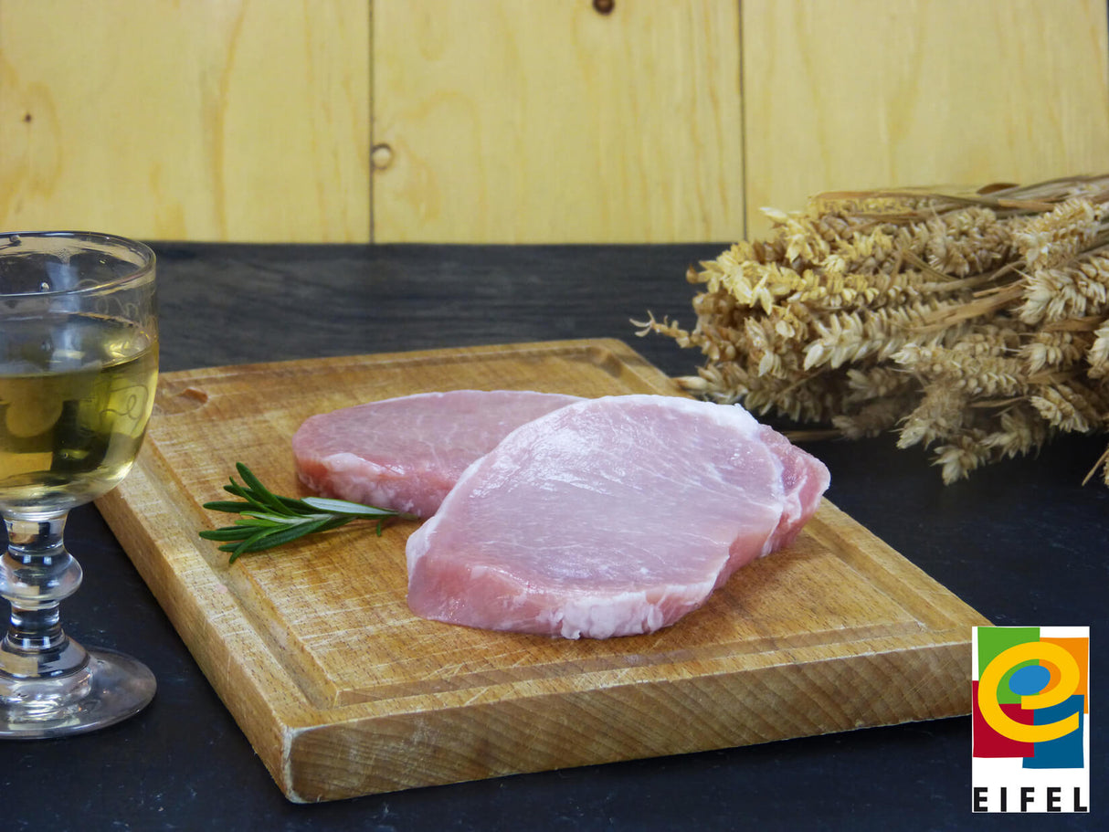 Rückensteak vom EIFEL Schwein auf Holzbrett mit Ähren und Weinglas vor Holzwand