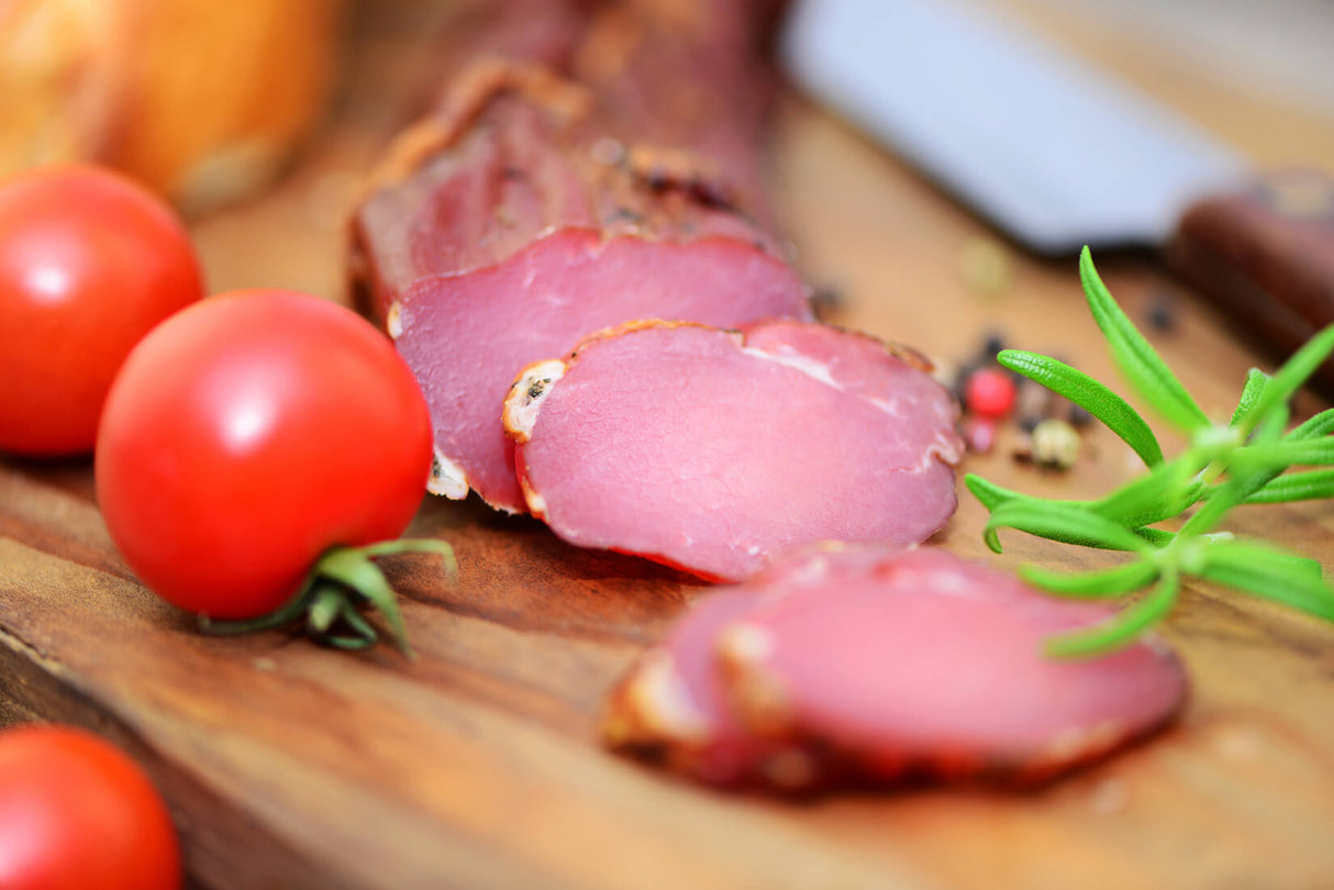 Räucherlende vom EIFEL Schwein angeschnitten auf Holzbrett mit Tomaten und Kräutern