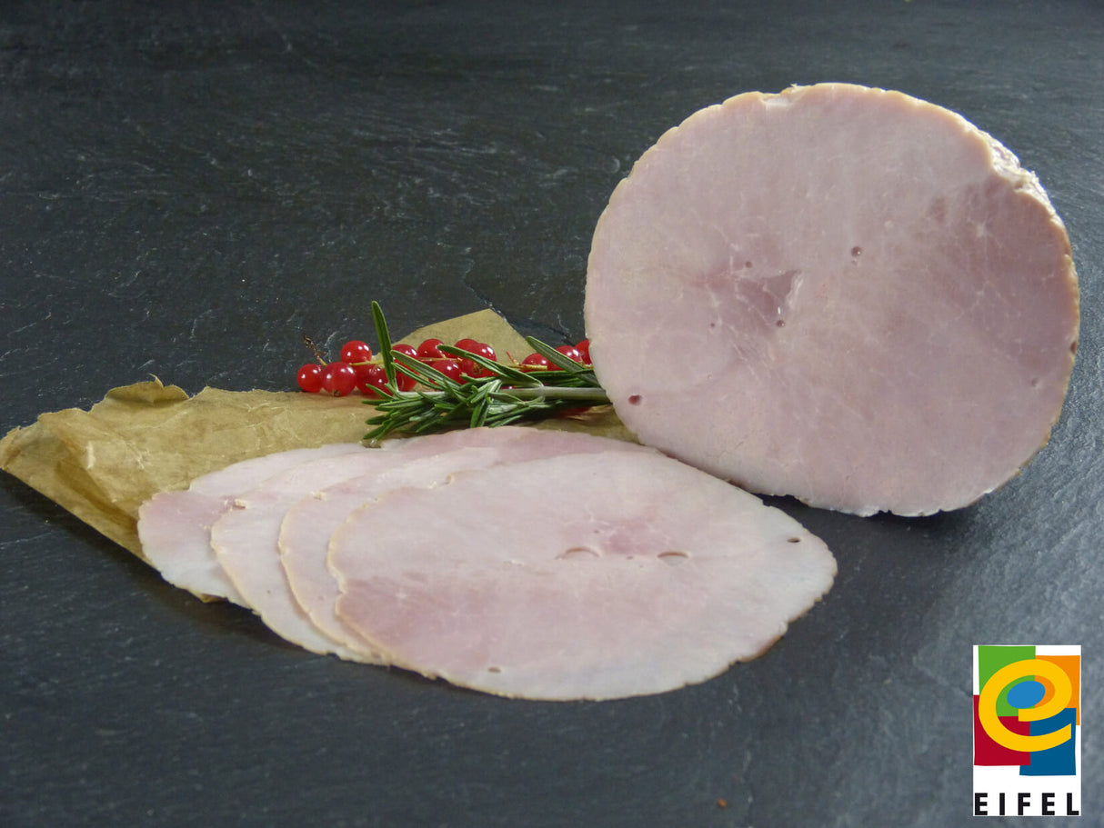 Kochschinken aus der Oberschale vom EIFEL Schwein ganz und aufgeschnitten angerichtet auf Backpapier mit Rosmarin und Preiselbeeren auf Schieferhintergrund