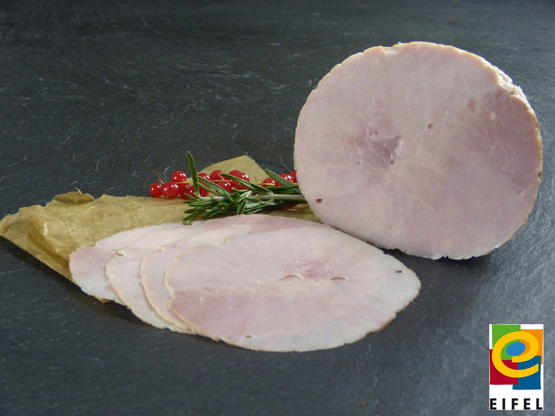 Kochschinken aus der Oberschale vom EIFEL Schwein ganz und aufgeschnitten angerichtet auf Backpapier mit Rosmarin und Preiselbeeren auf Schieferhintergrund