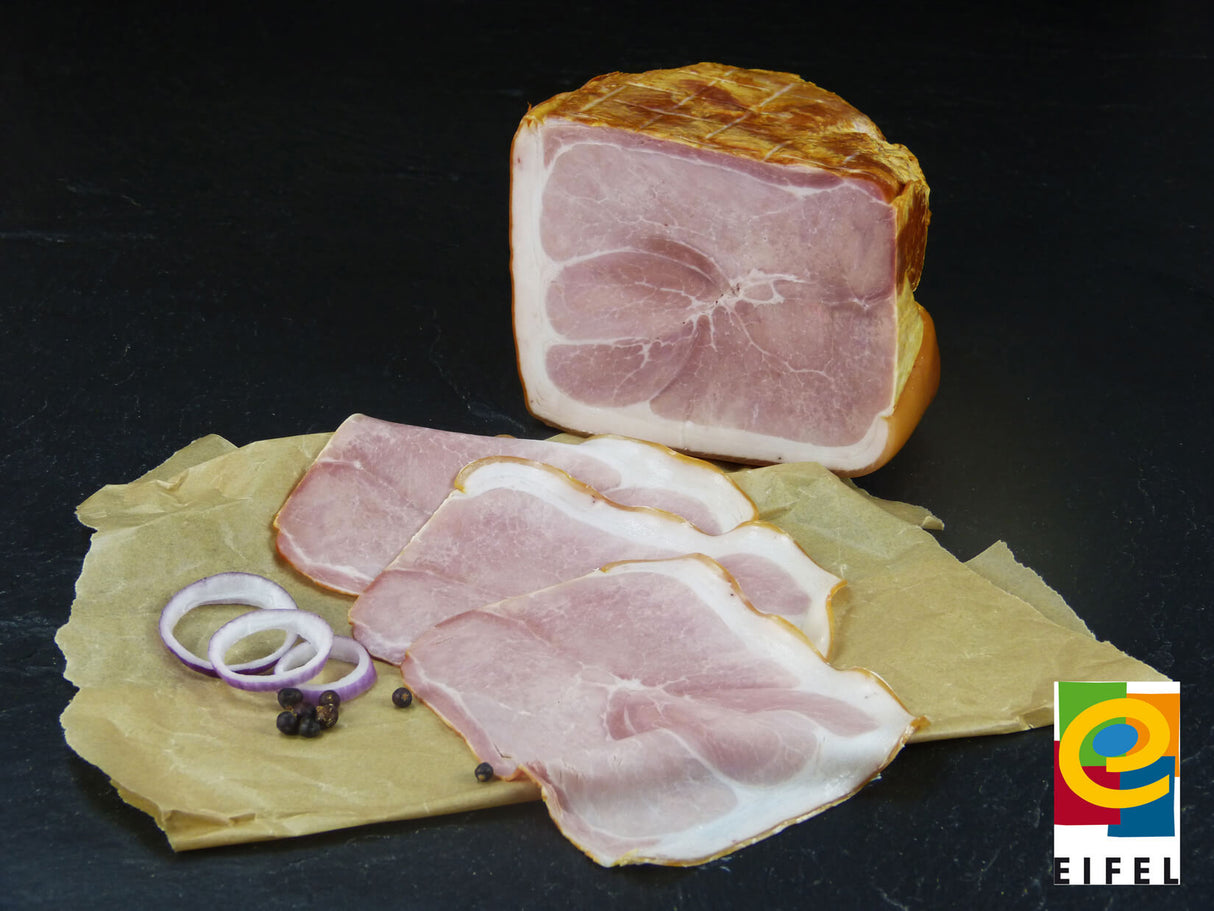 Metzgerschinken vom EIFEL Schwein und Scheiben mit roten Zwiebeln und Wachholderbeeren mit Ähren auf Schieferhintergrund