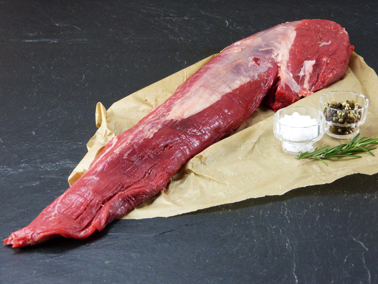 Färsenfilet aus der Eifel angerichtet auf Backpapier mit Salz und Pfefferkörnern und Rosmarin auf Schieferhintergrund