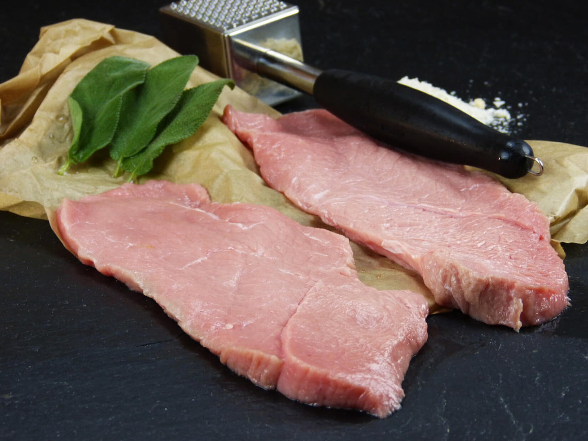 Kalb Oberschalenschnitzel angerichtet auf Backpapier mit Salbei und einem Fleischklopfer auf Schieferhintergrund