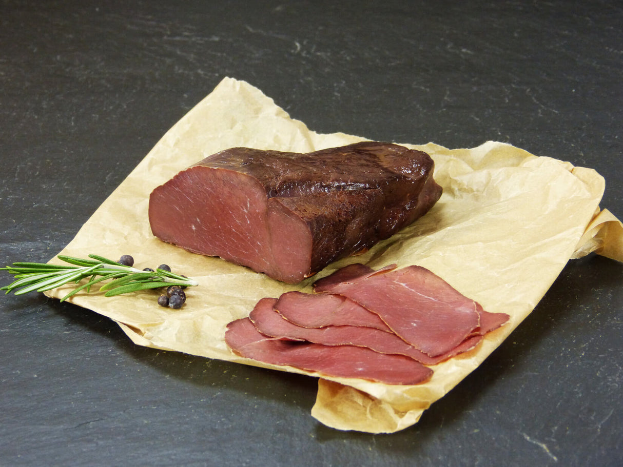 Hirschschinken vom EIFEL Wild auf Backpapier angerichtet mit Kräutern auf Schieferhintergrund