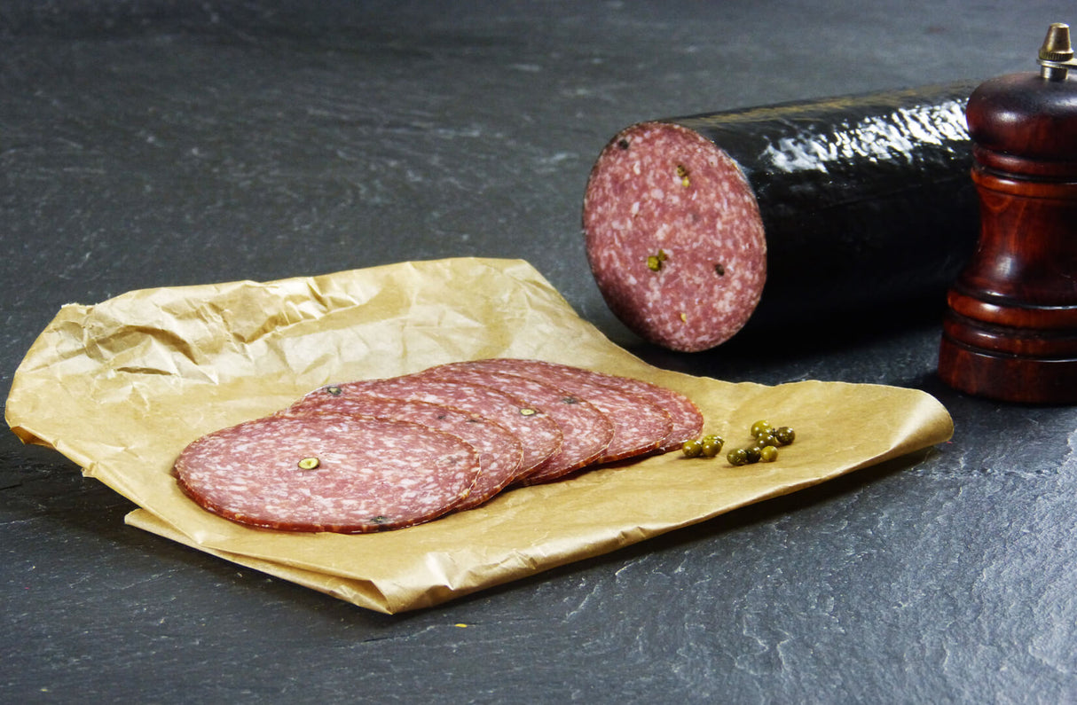 Pfeffersalami geschnitten mit grünem Pfeffer und Pfeffermühle auf Schieferhintergund