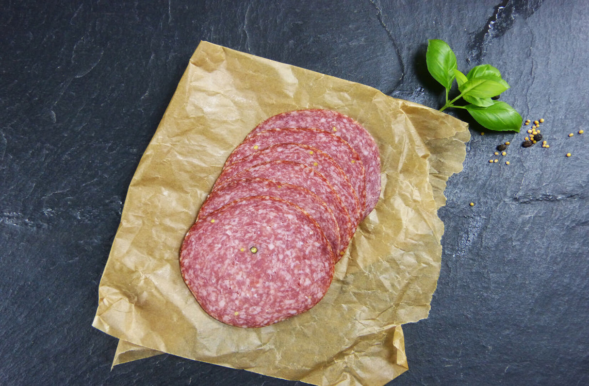 Land Cervelatwurst geschnitten mit Pfeffer und Basilikum auf Schieferhintergung