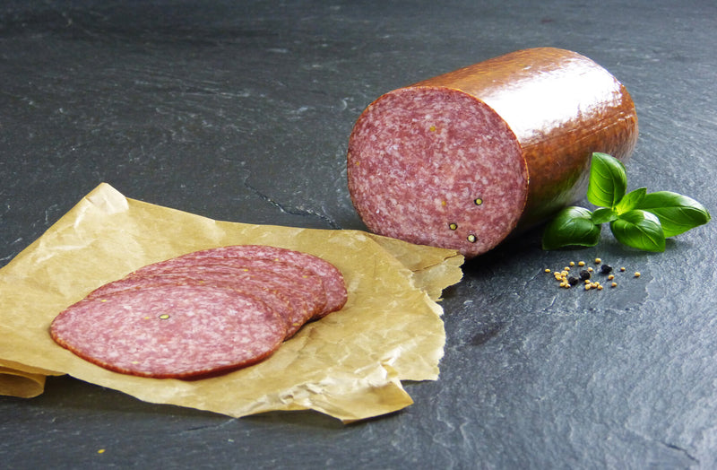 Land Cervelatwurst geschnitten mit Pfeffer und Basilikum auf Schieferhintergrund
