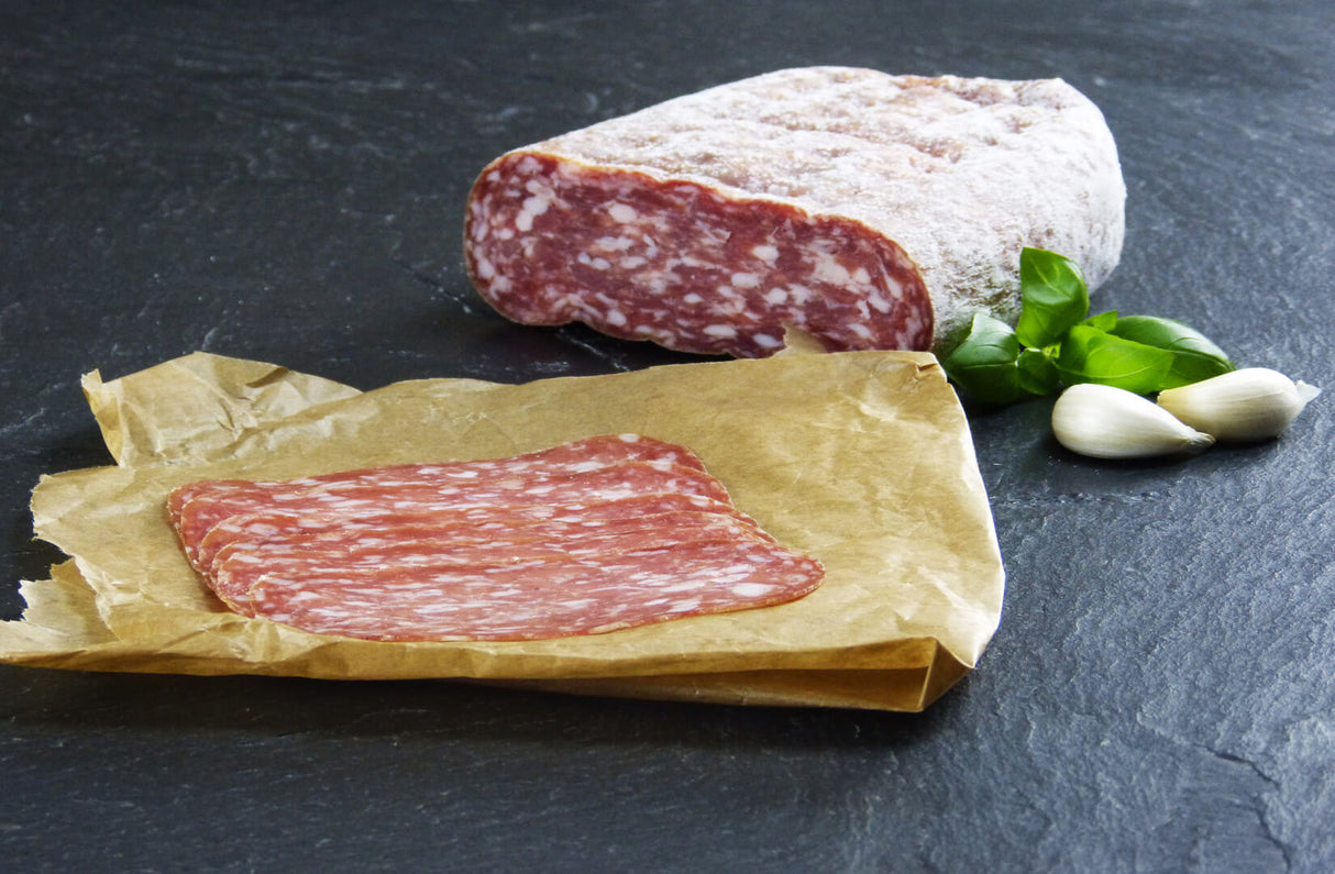 Salami Spianata Romana geschnitten mit Basilikum und Knoblauch auf Schieferhintergrund