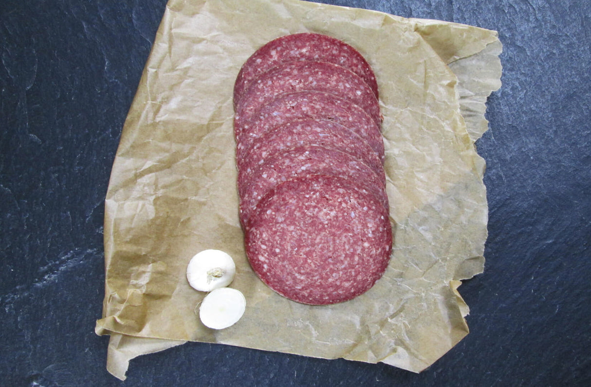 Rindersalami aufgeschnitten auf Backpapier auf Schieferhintergrund