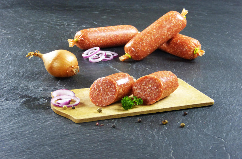 Zwiebelmettwurst auf Holzbrett angerichtet mit Petersilie Zwiebeln und Pfefferkörnern auf Schieferhintergrund